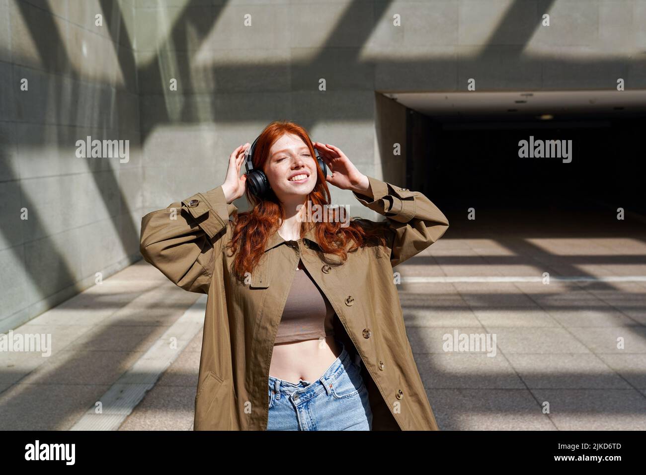 Ragazza felice teen redhead indossando le cuffie ascoltare musica vicino alle pareti urbane. Foto Stock