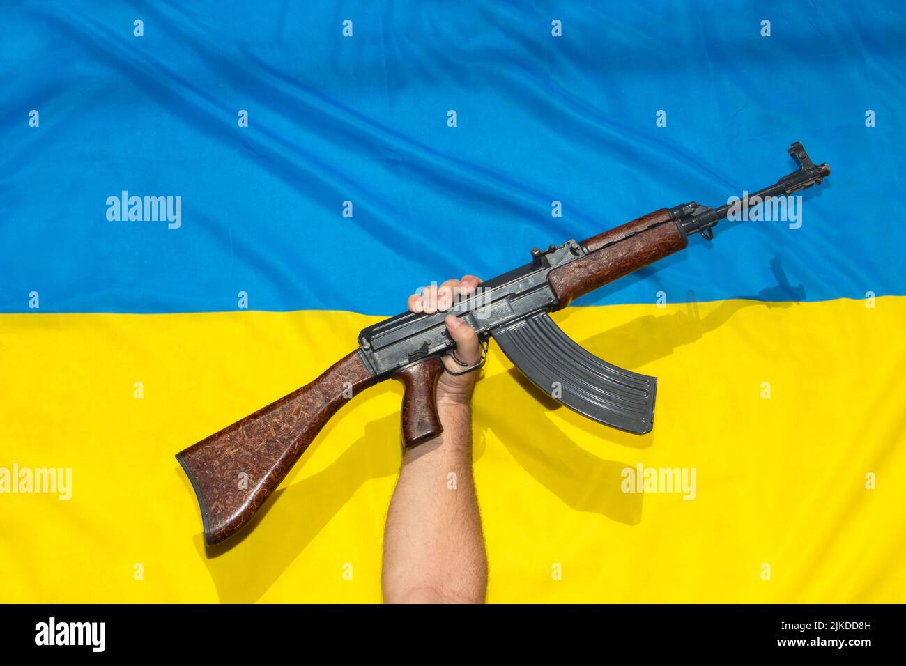 La pistola sollevata davanti alla bandiera Ucraina, simboleggia la resistenza contro l'aggressore Foto Stock