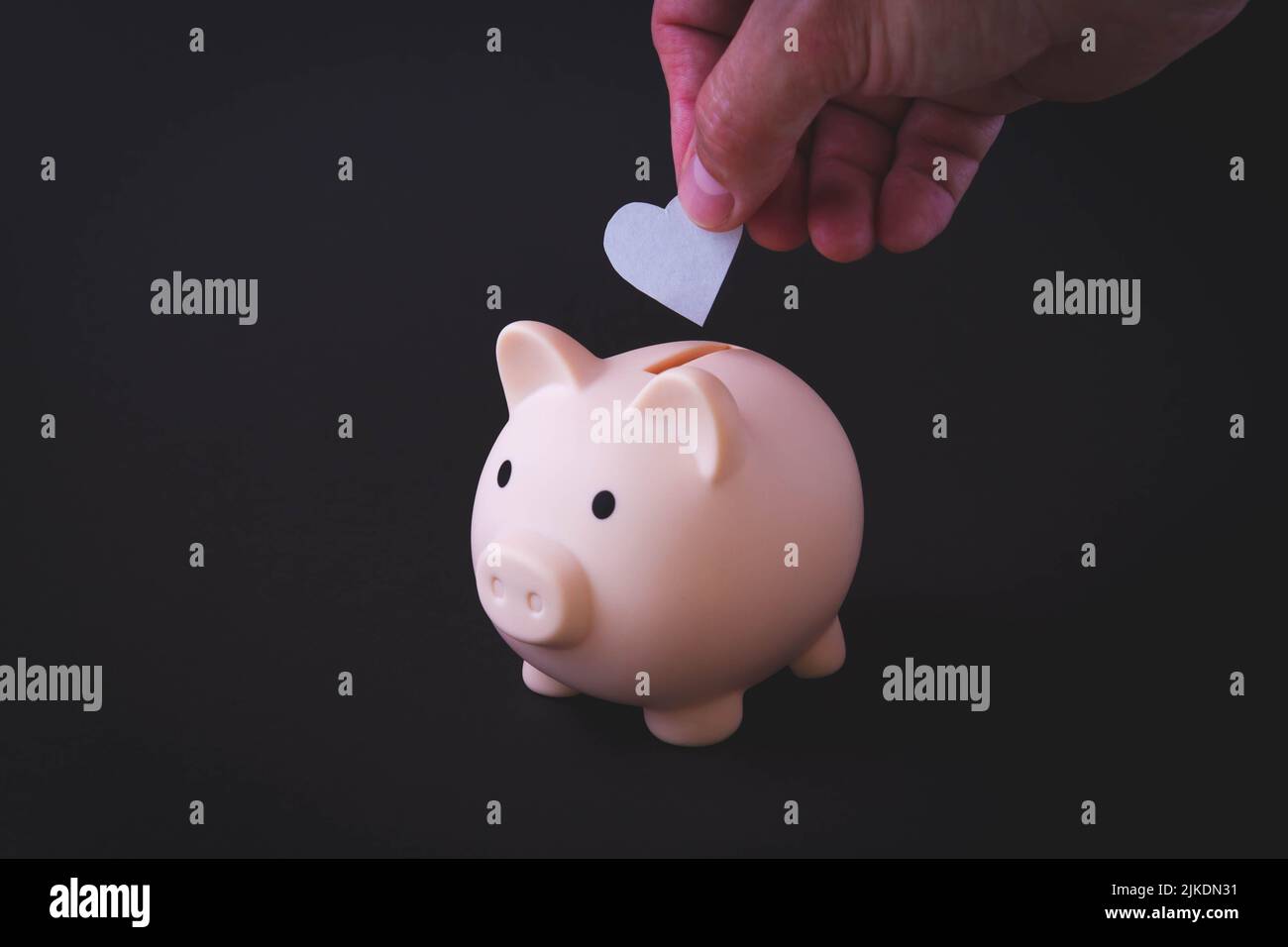 Risparmiare denaro. La mano mette un cuore in una banca piggy. Mantenimento dello stipendio. Investimento redditizio. La salute nella banca del piggy. Foto di alta qualità Foto Stock