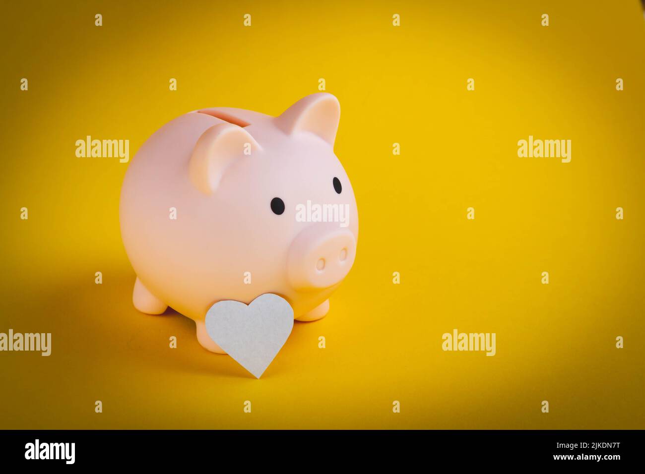 Risparmiare denaro. La mano mette un cuore in una banca piggy. Mantenimento dello stipendio. Investimento redditizio. La salute nella banca del piggy. Foto di alta qualità Foto Stock