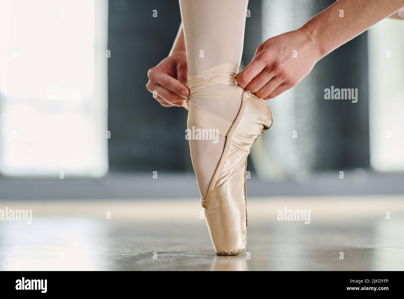 Mani di ballerina legano nastri di seta di scarpe pointe mantenendo il piede sulla punta del piede sul pavimento della sala da ballo o dell'aula per le ripetizioni Foto Stock