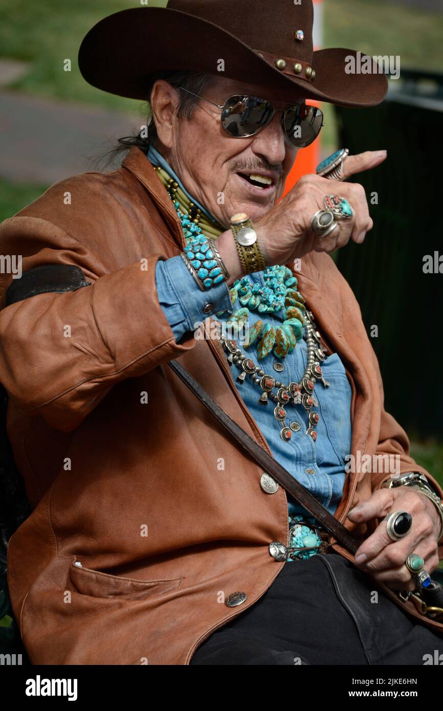 Un uomo che indossa una varietà di gioielli nativi americani, tra cui collane, bracciali e anelli, siede su una panchina a Santa Fe, New Mexico. Foto Stock