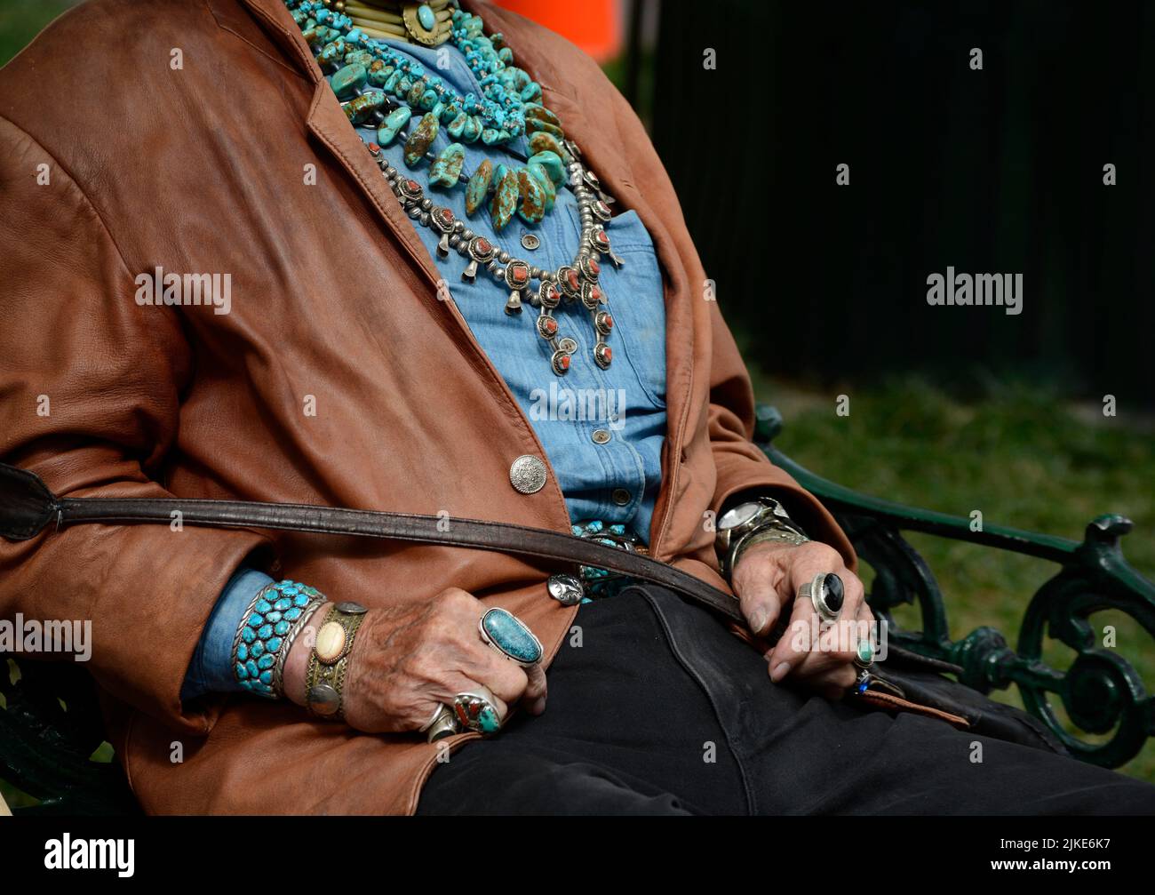 Un uomo che indossa una varietà di gioielli nativi americani, tra cui collane, bracciali e anelli, siede su una panchina a Santa Fe, New Mexico. Foto Stock