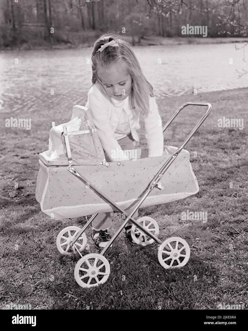 1960S RAGAZZA BIONDA PICCOLA IN CORTILE TENDENTE ALLA SUA BAMBOLA IN UNA CARROZZA TOY BAMBINO - J12172 HAR001 HARS COPIA SPAZIO MEZZO-LUNGO FLUSSO CURA B&W CARROZZA SOGNI MATERNI FELICITÀ ALTO ANGOLO FEMMINILE IMMAGINAZIONE RUOLO GIOCARE BAMBINO BUGGY GENDER GROWTH GIOVANI BABY CARROZZA BIANCA E NERA ETNIA CAUCASICA HAR001 VECCHIO STILE TENDENTE Foto Stock