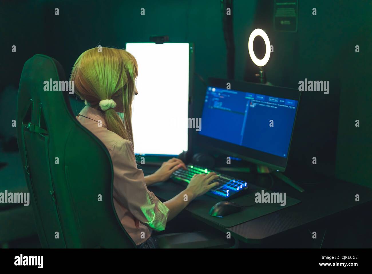 Ragazza bianca adolescente che indossa graziosi ponytail seduti in sedia da gioco utilizzando un computer professionale con luce ad anello. Illuminazione verde scuro. Foto di alta qualità Foto Stock