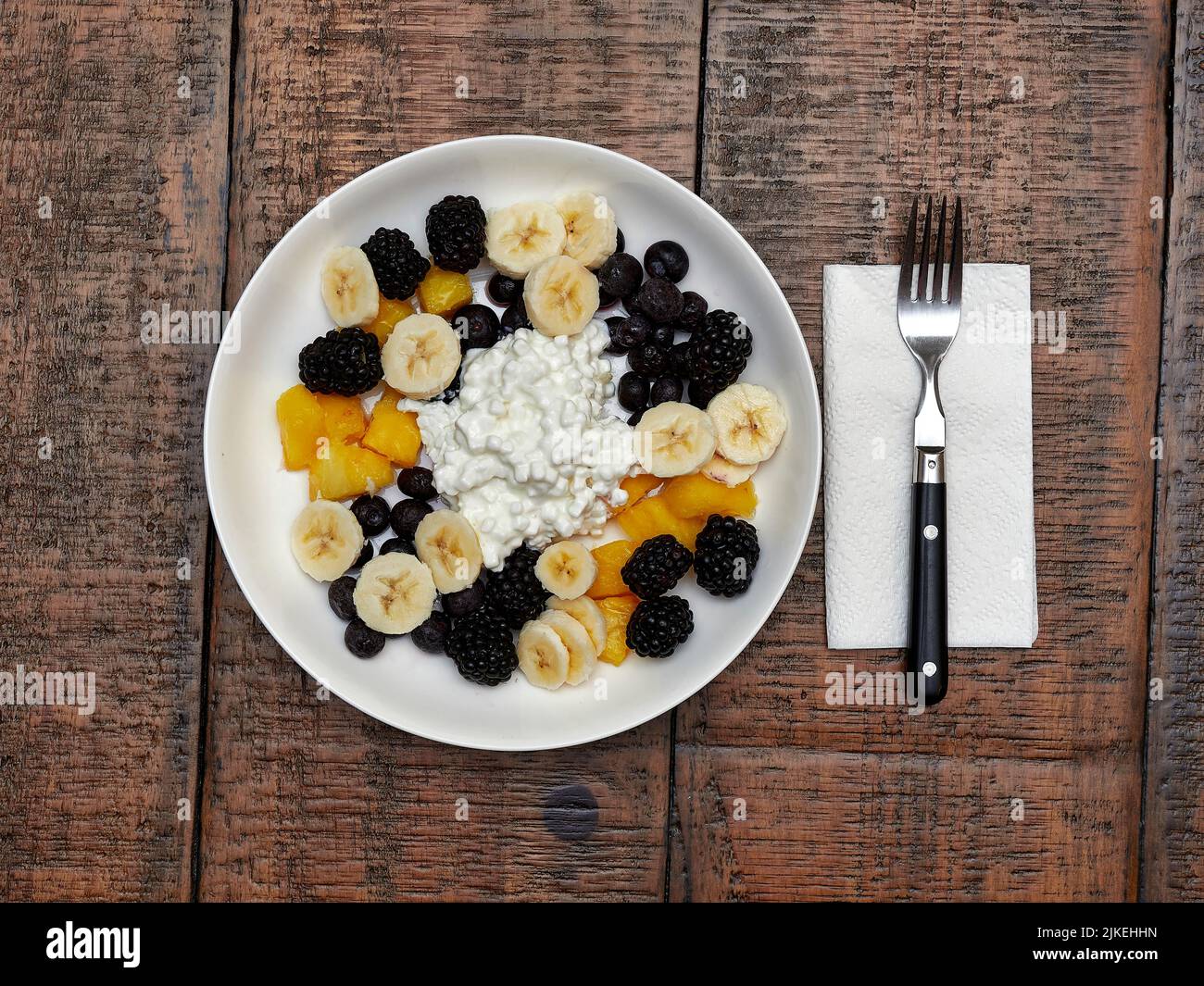 Pasto sano per la colazione o pranzo ciotola di formaggio cottage e frutta composta da fette di banana, mirtilli e more, vista dall'alto. Foto Stock