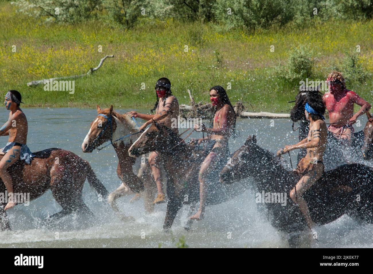 I coraggiosi indiani americani corrono in guerra a cavallo attraversando il fiume Little Bighorn durante la rievocazione annuale di Custer's Last Stand, Montana Foto Stock