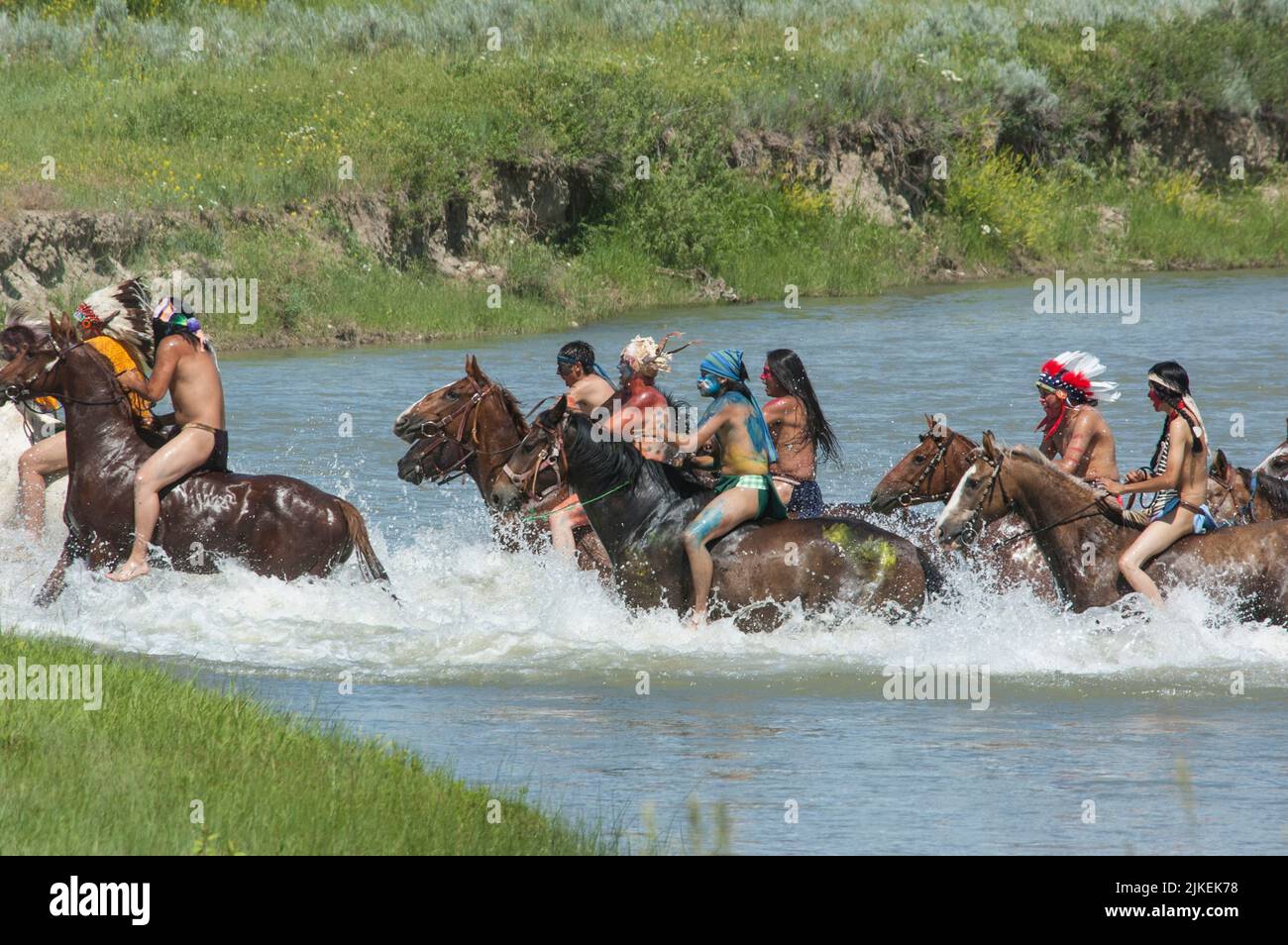 I coraggiosi indiani americani corrono in guerra a cavallo attraversando il fiume Little Bighorn durante la rievocazione annuale di Custer's Last Stand, Montana Foto Stock