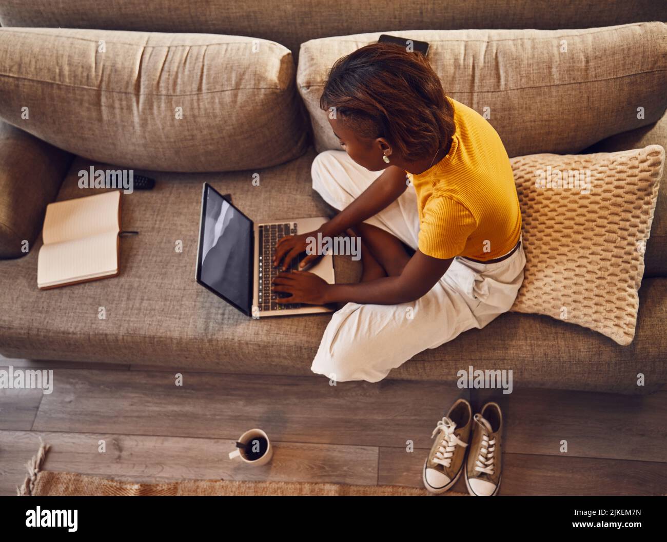 Apprendimento a distanza dello studente scrivere, studiare e digitare su un laptop facendo un test di assegnazione virtuale sul divano a casa. Sopra la vista di una giovane femmina Foto Stock