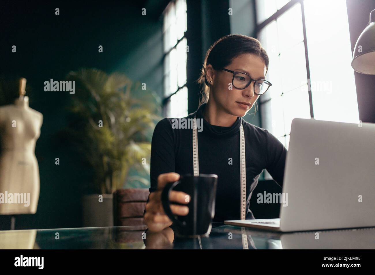 Designer di abbigliamento femminile che utilizza un computer portatile in ufficio. Donna impegnata che lavora su un notebook in studio. Foto Stock