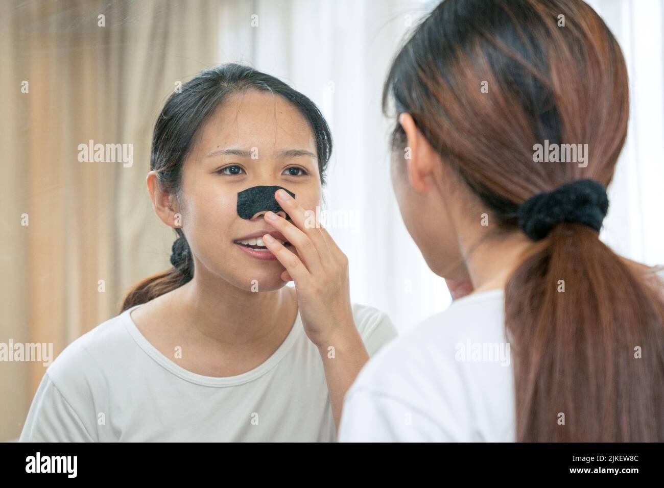 Bella donna asiatica guardando lo specchio, applicando maschera carbone pulizia profonda naso poro striscia su pelle fresca pulita. Trattamento di bellezza e cura della pelle Foto Stock