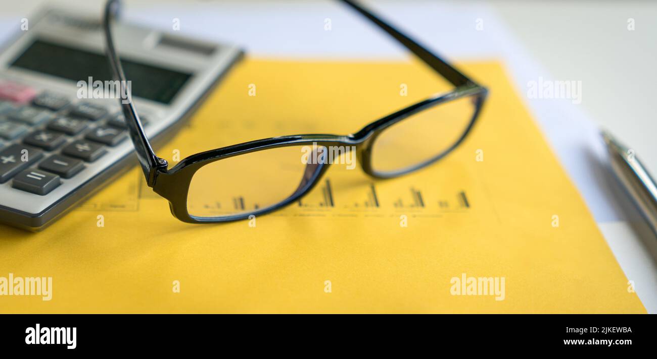 Occhiali, calcolatrice e penna in cima al report con grafici. Concetto di contabilità finanziaria e tendenze del mercato. Foto Stock