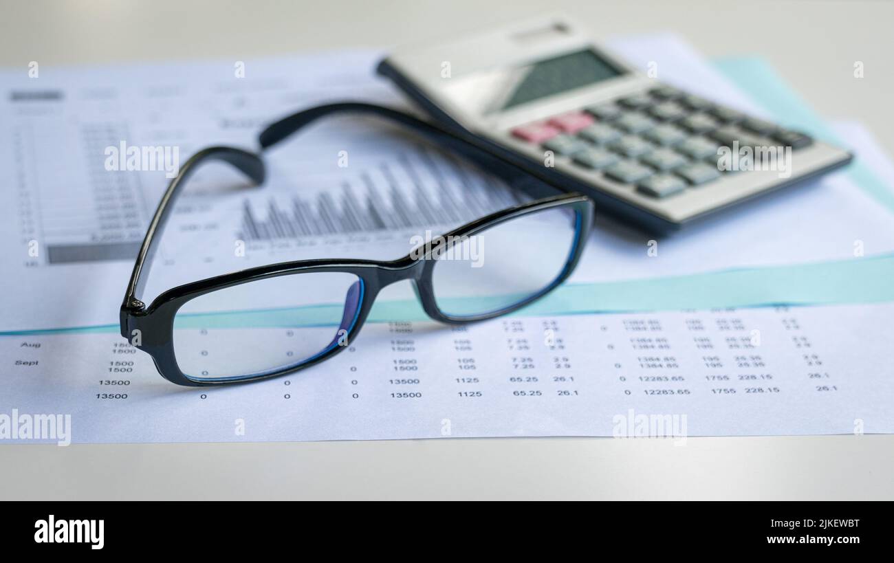 Occhiali e calcolatrice in cima a report e grafici finanziari. Concetto di contabilità finanziaria e tendenze del mercato. Foto Stock