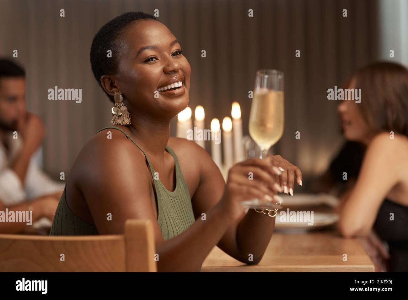 Questo buon umore è stato sponsorizzato da Bubbly. Una giovane donna attraente seduta con i suoi amici durante una festa a cena e gustare un bicchiere di champagne. Foto Stock