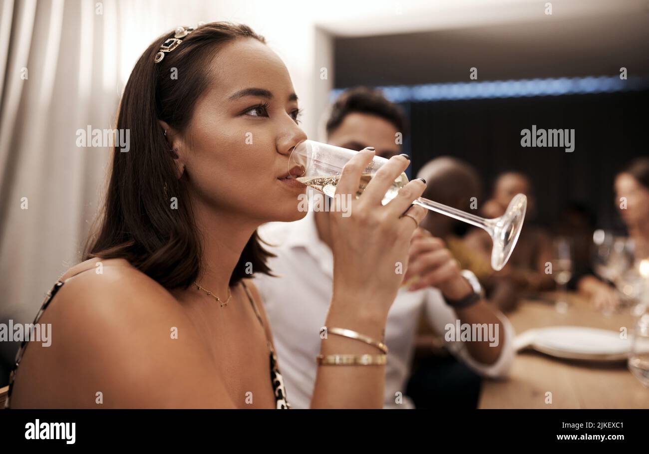 Ho bisogno di un po' di coraggio liquido: Una giovane donna attraente che siede e beve champagne in una cena di Capodanno con gli amici. Foto Stock