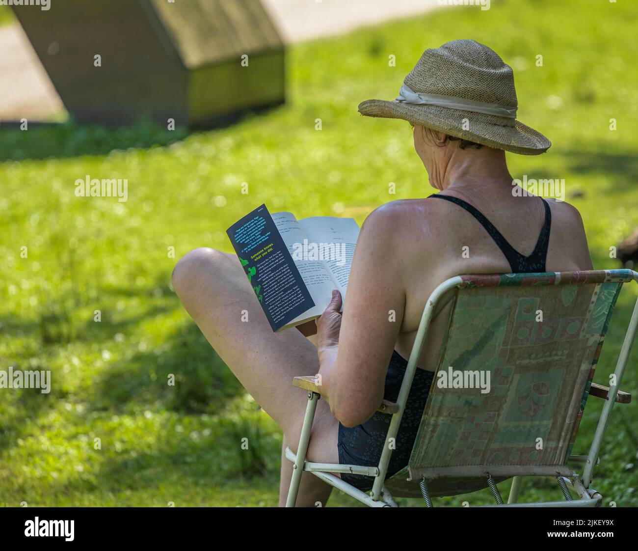 Donna anziana seduta sulla sedia da spiaggia sulla spiaggia e lettura di un libro. Donna anziana riposante sul mare rilassarsi e godere di attività all'aperto stile di vita in sintesi Foto Stock