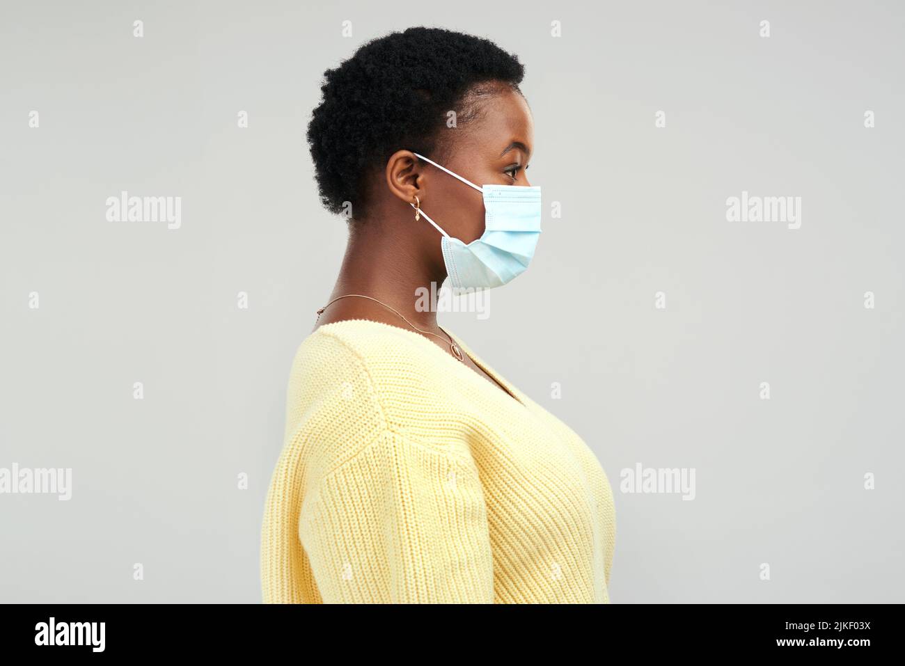 Si prega di indossare la maschera. Una giovane donna che indossa una maschera chirurgica in piedi su uno sfondo grigio. Foto Stock