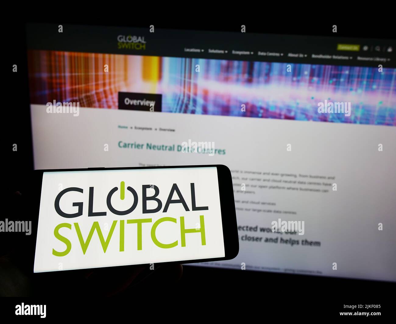 Persona che tiene il cellulare con il logo della società britannica di data center Global Switch Limited sullo schermo di fronte alla pagina web. Mettere a fuoco sul display del telefono. Foto Stock