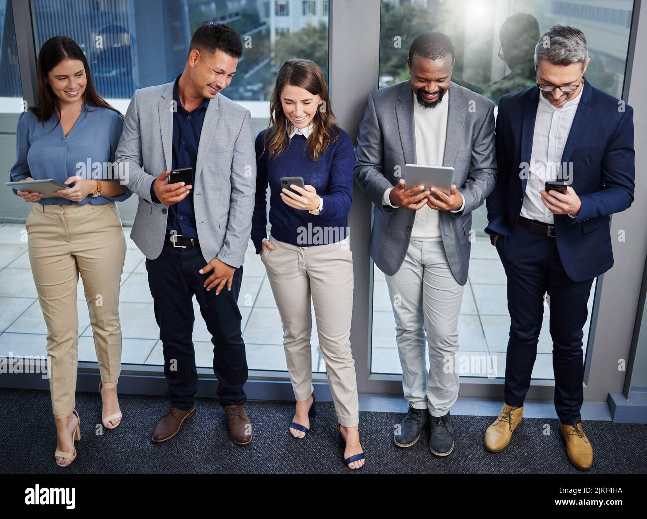 Lavoriamo sempre meglio insieme. Un gruppo di giovani imprenditori che utilizzano dispositivi digitali mentre attendono in linea. Foto Stock