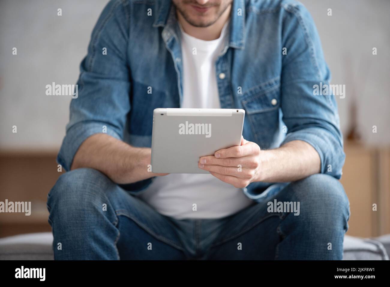 Uomo che trascorre tempo con il tablet digitale a casa, leggendo notizie, navigando in Internet, guardando video, controllando i social network mentre si rilassa sul divano in L. Foto Stock