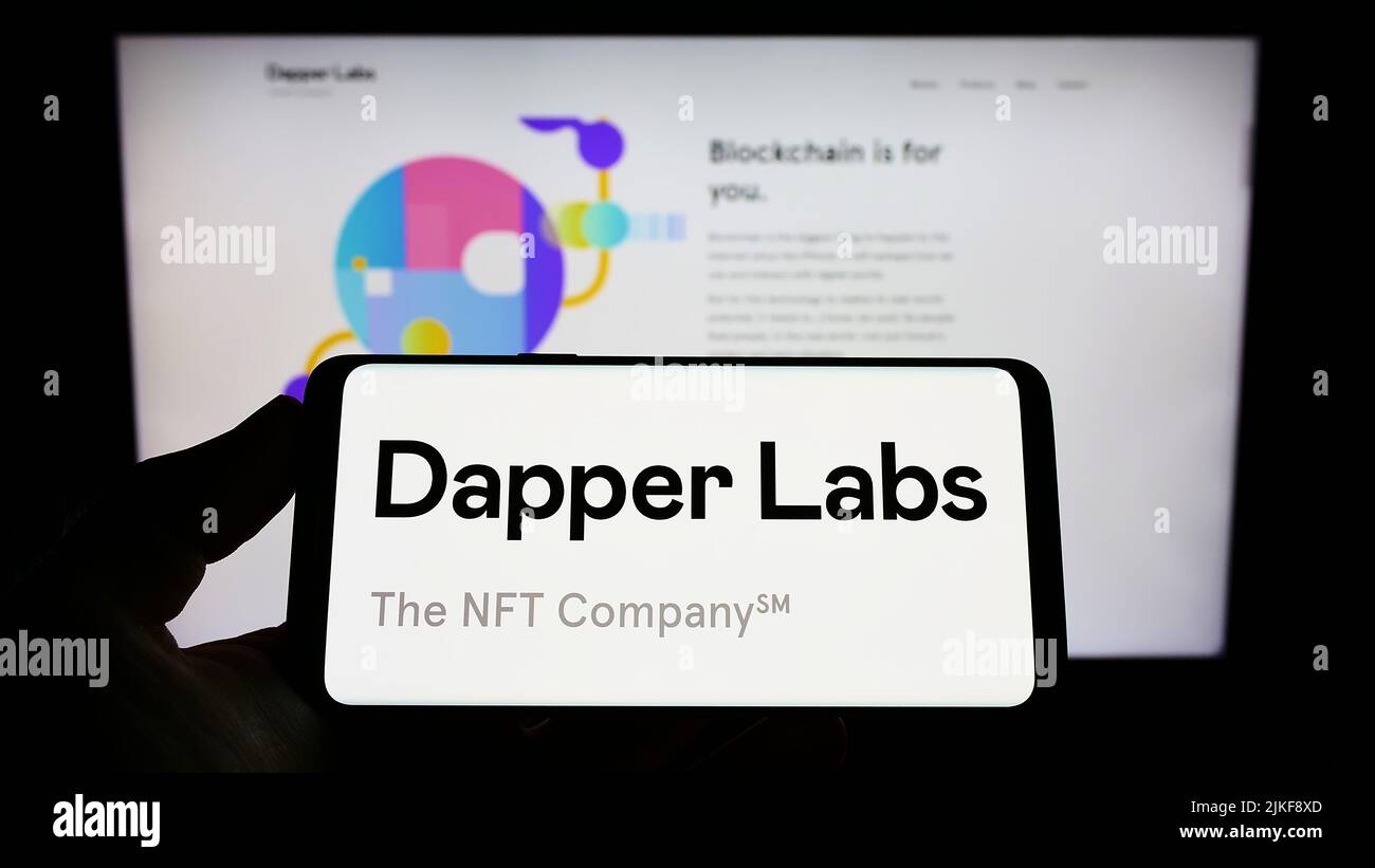 Persona che tiene uno smartphone con il logo della società canadese Dapper Labs Inc. Sullo schermo di fronte al sito Web. Mettere a fuoco sul display del telefono. Foto Stock