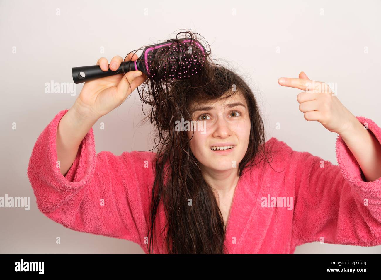 Una donna cerca di pettinare i capelli bagnati aggrovigliati. Cura dei capelli a casa, perdita dei capelli e sezione. Foto Stock