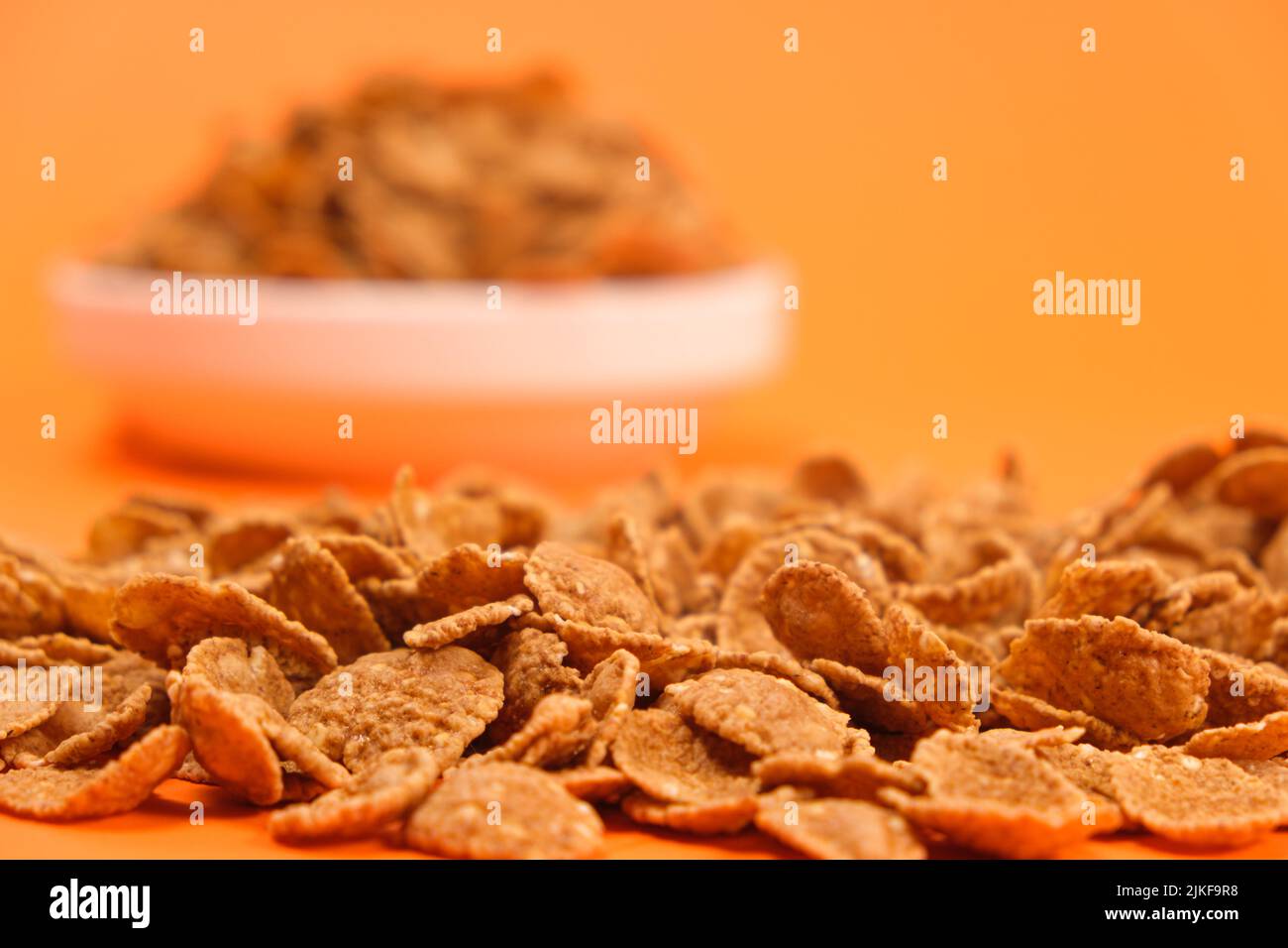 Primo piano di fiocchi di grano su sfondo arancione, veloce cereali salubre colazioni Foto Stock