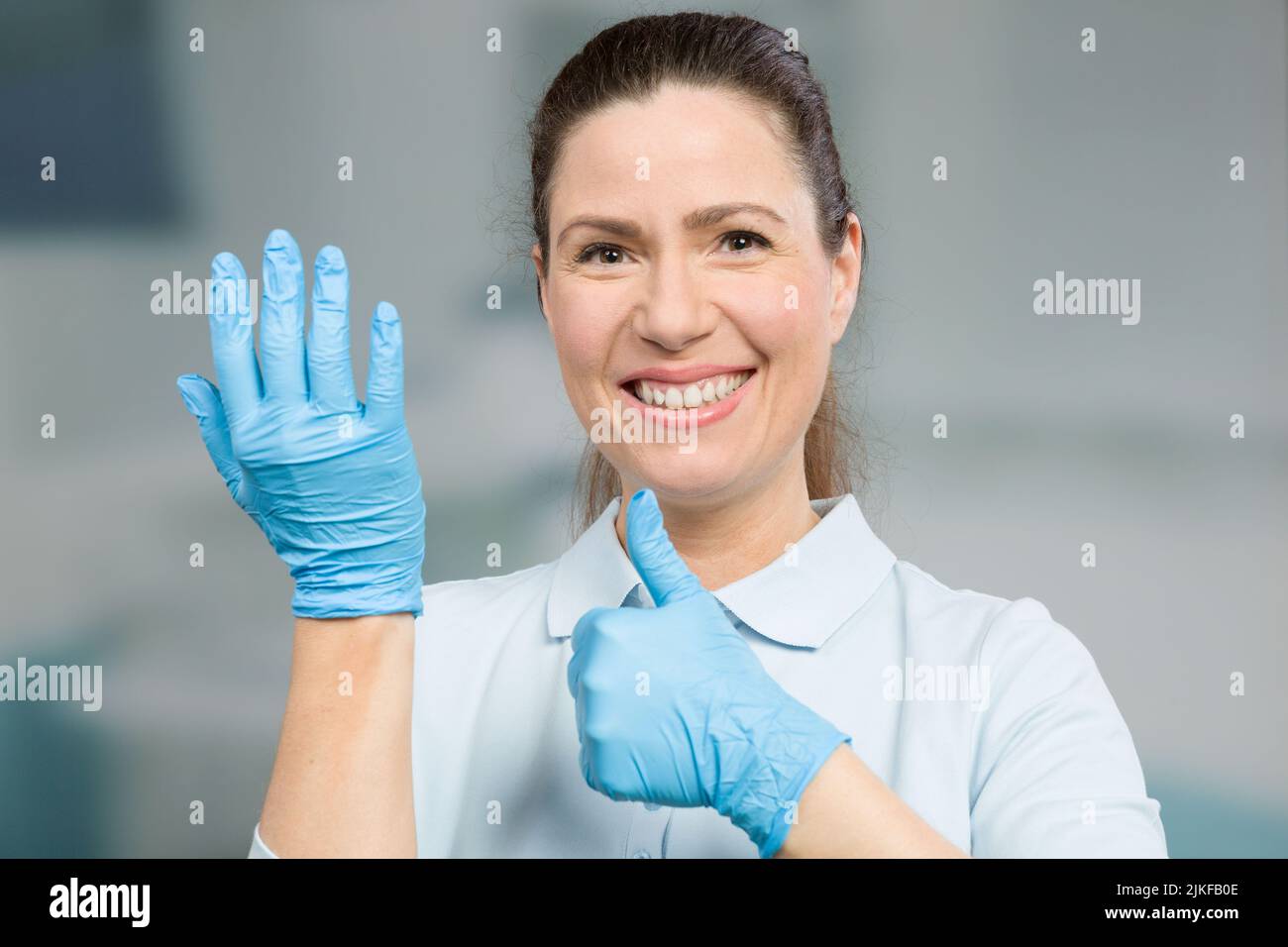 medico o infermiera femminile indossa i guanti medici e mostra i pollici Foto Stock