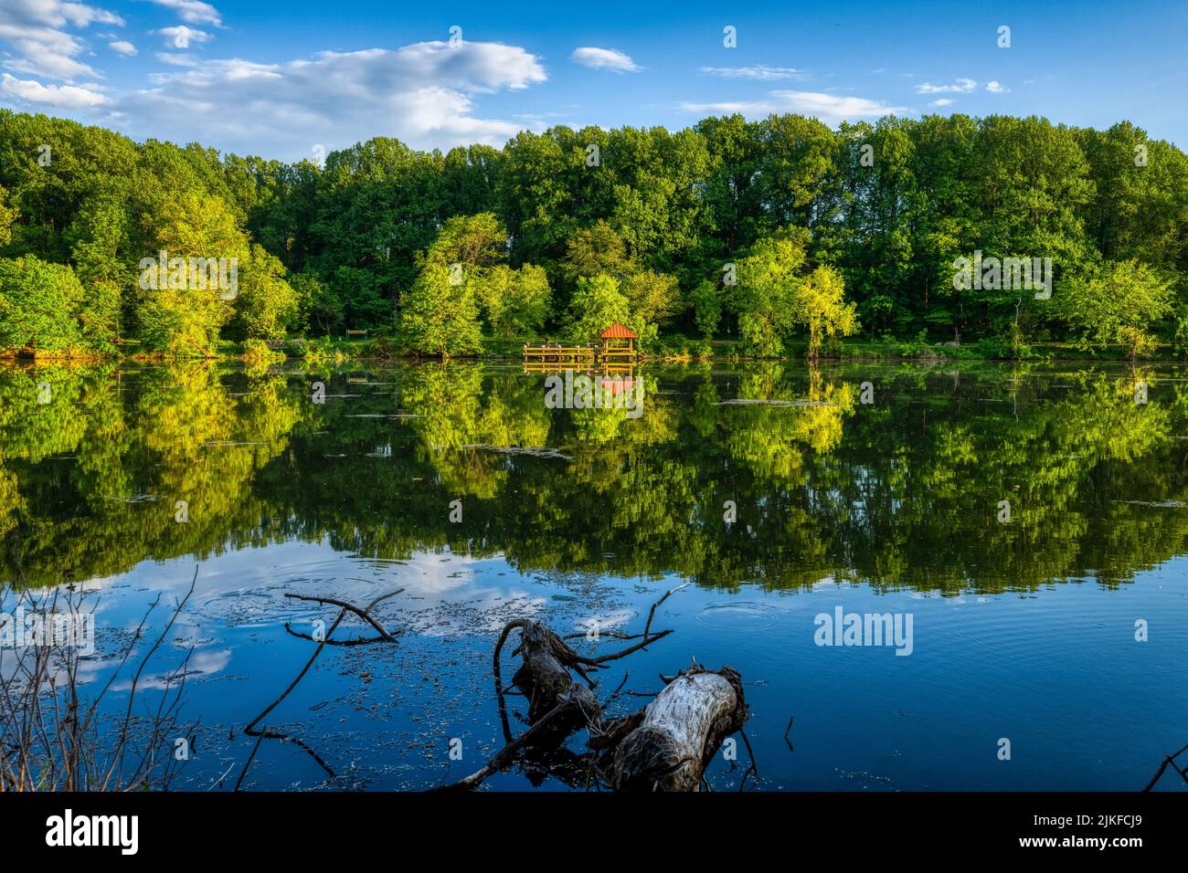 Una vista panoramica di un lago tranquillo che riflette un'alcova in legno e il verde sulla sua riva Foto Stock