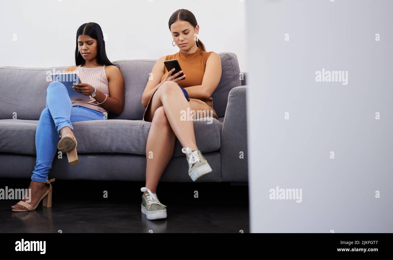 Un passo più vicino alla nostra carriera da sogno: Due giovani donne che usano i loro dispositivi in attesa di essere intervistate in un ufficio moderno. Foto Stock