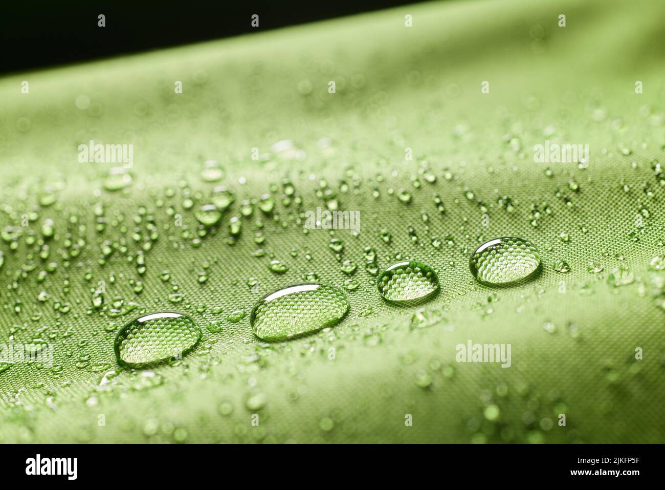Primo piano abbondanza di gocce d'acqua pulita trasparente su tessuto impregnato verde acqua testurizzata su sfondo sfocato in ambienti luminosi Foto Stock