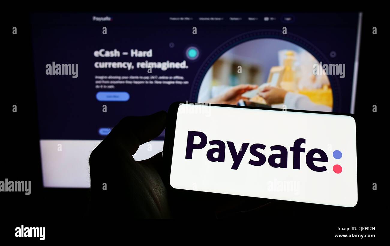 Persona che tiene uno smartphone con il logo della società di pagamenti britannica Paysafe Group sullo schermo di fronte al sito web. Mettere a fuoco sul display del telefono. Foto Stock