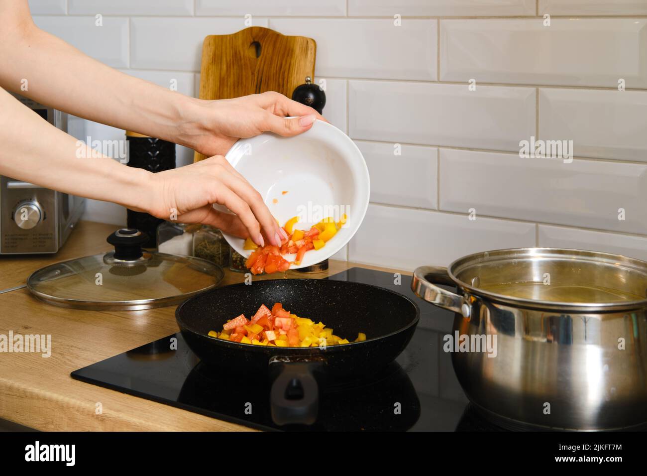 La vista closeup della mano femminile mette le verdure tritate in una padella. Processo di preparazione del sugo di verdure. Foto Stock