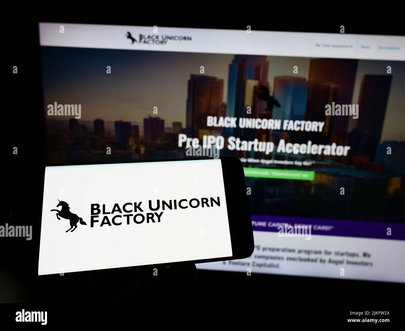 Persona che detiene il telefono cellulare con il logo della società di capitali di rischio statunitense Black Unicorn Factory sullo schermo di fronte alla pagina web. Mettere a fuoco sul display del telefono. Foto Stock