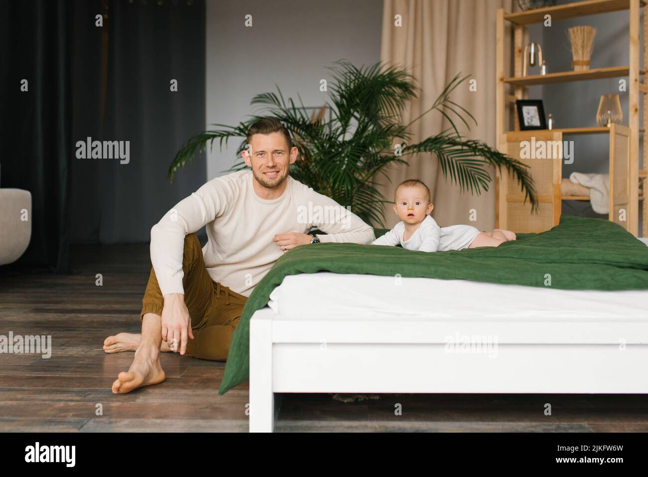 Un giovane padre è appeso vicino al letto sul quale è adagiato il figlio Foto Stock