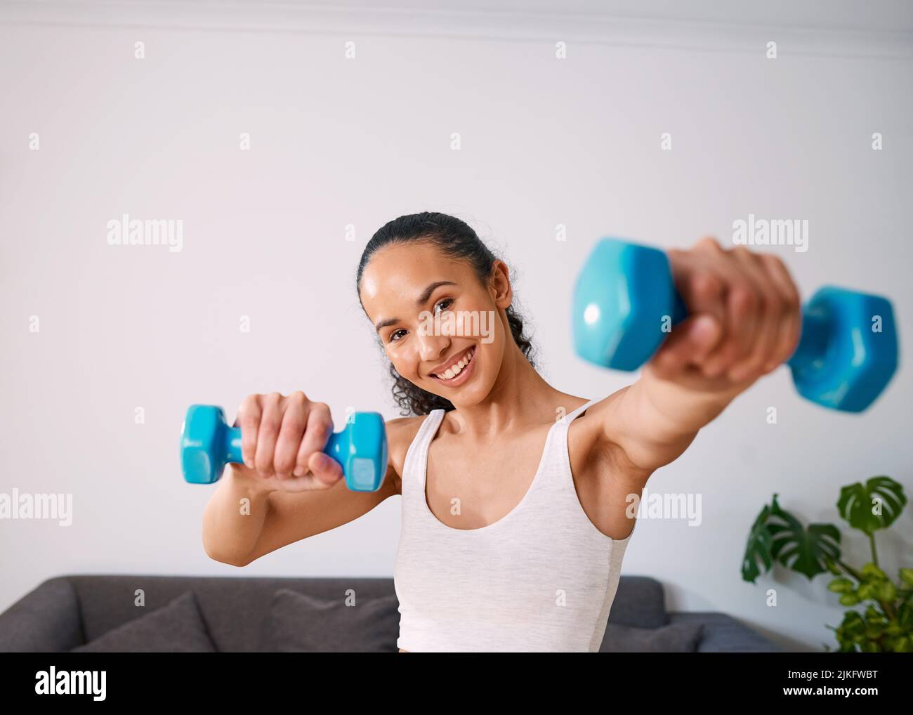 Una giovane donna sorride mentre tiene 2kg pesi a casa Foto Stock