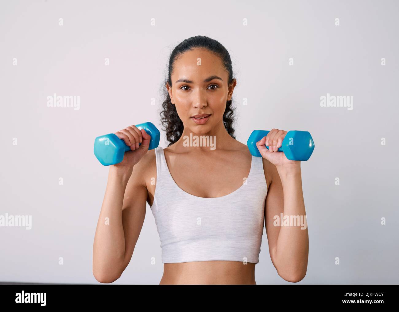 Una giovane donna seria solleva piccoli pesi per diventare forte a casa Foto Stock