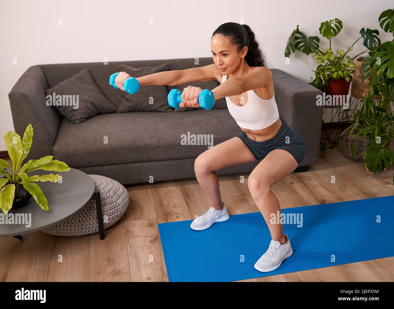 Una giovane donna squats e solleva i pesi a casa ottenendo in forma Foto Stock