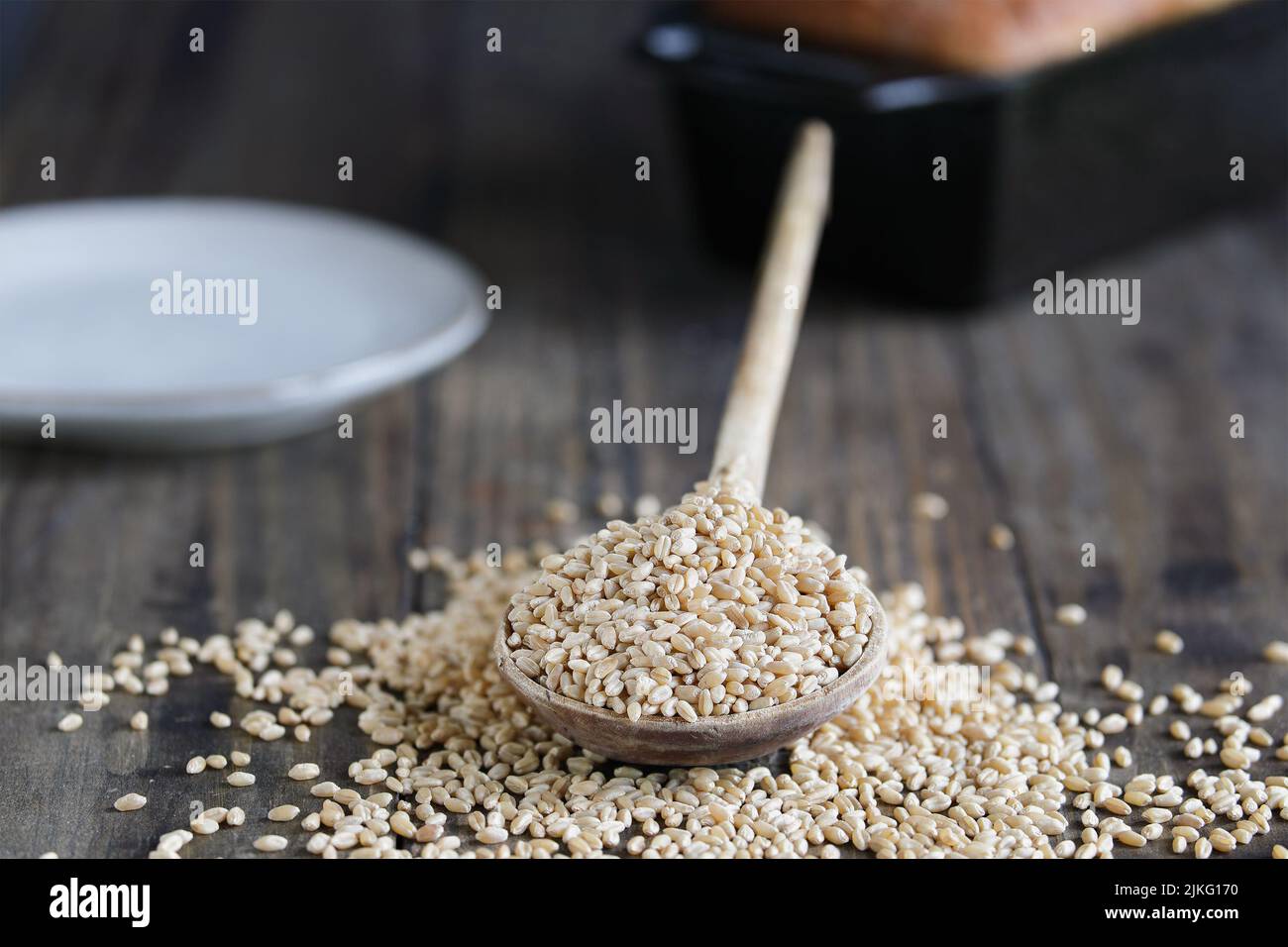 Cucchiaio di legno riempito con bacche di grano duro bianco. Messa a fuoco selettiva con primo piano e sfondo sfocati. Pane di sottofondo. Foto Stock