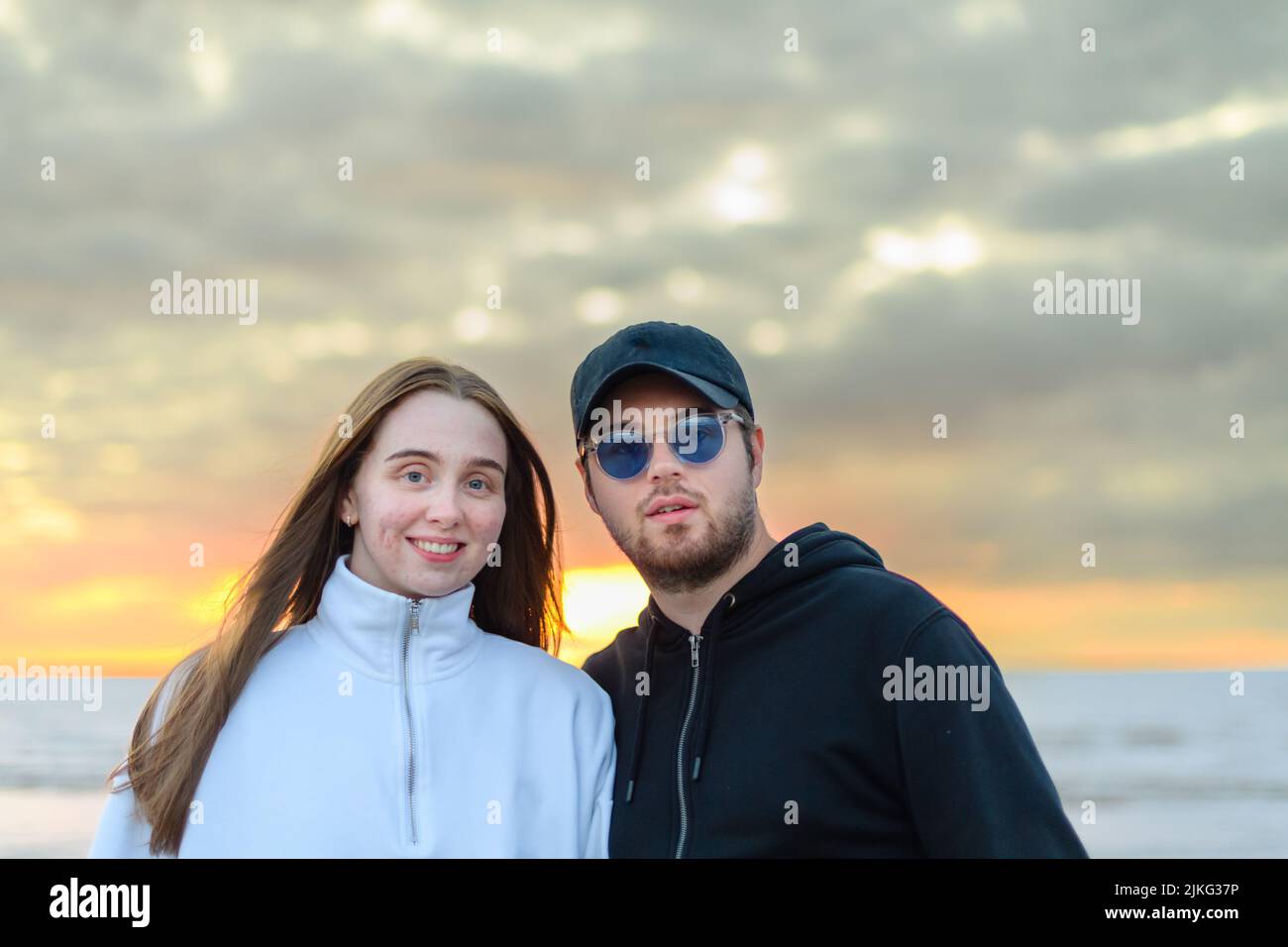 Una giovane e felice coppia caucasica che si posa vicino al mare al tramonto Foto Stock