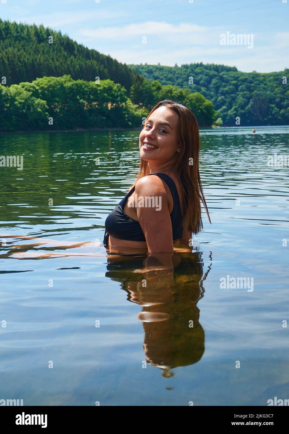 Una foto verticale di una ragazza ispanica sorridente e attraente che si posa in un lago Foto Stock