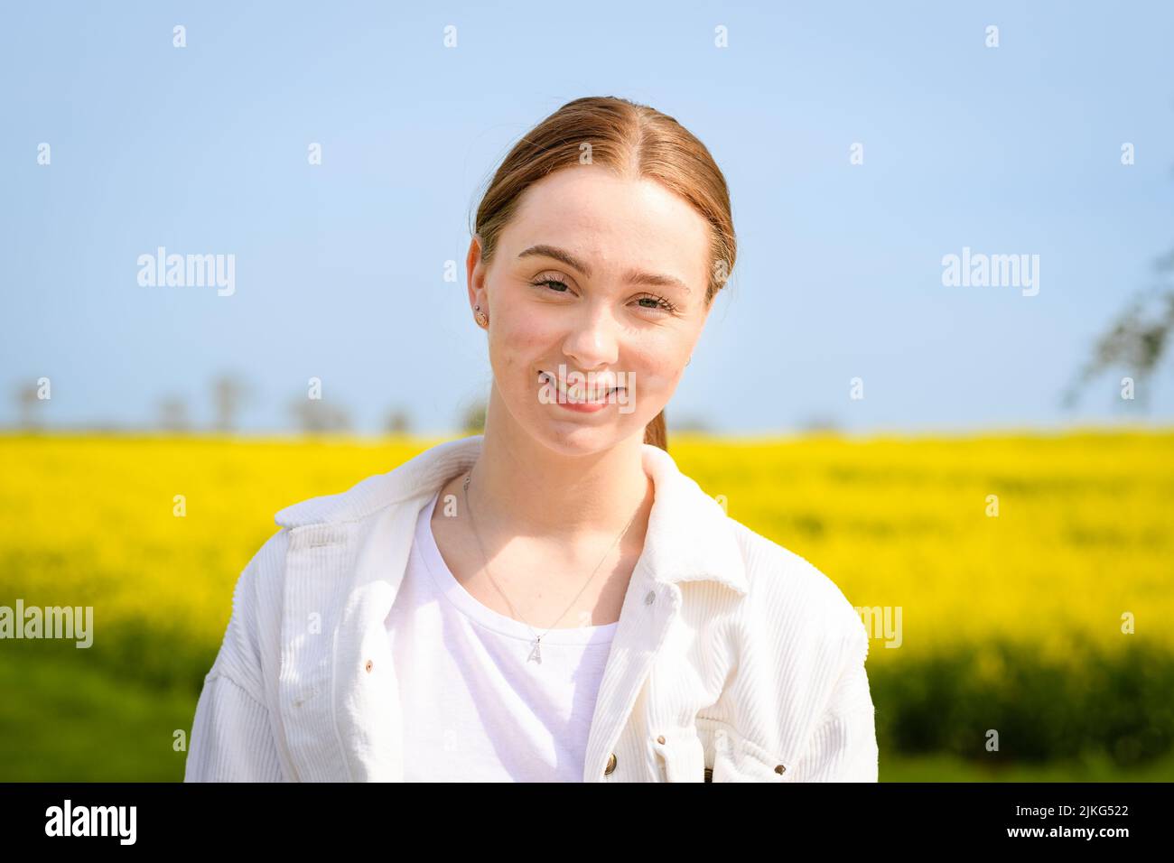 Un ritratto di una bella ragazza caucasica sorridente con capelli rossi nel campo della senape bianca Foto Stock