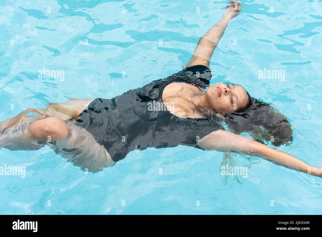 Donna serena in verdeggiante bikini galleggiante nella soleggiata piscina estiva Foto Stock