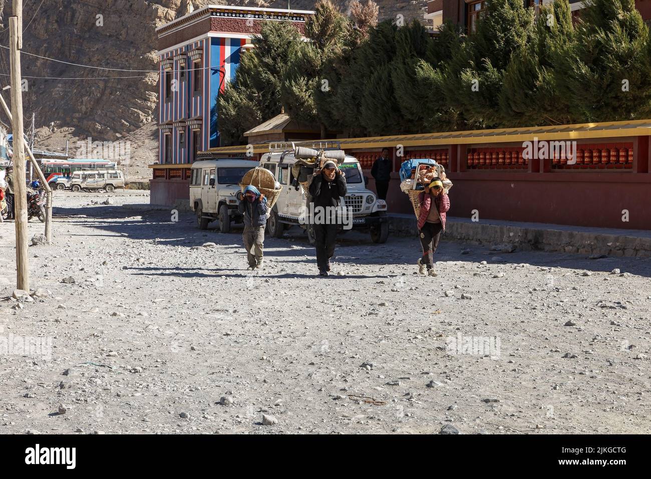 Jomsom, Nepal - 23 novembre 2016: Tre Porters che trasportano carichi pesanti. Tre uomini nepalesi camminano lungo la strada nella città di Jomsom vicino a un Buddha Foto Stock