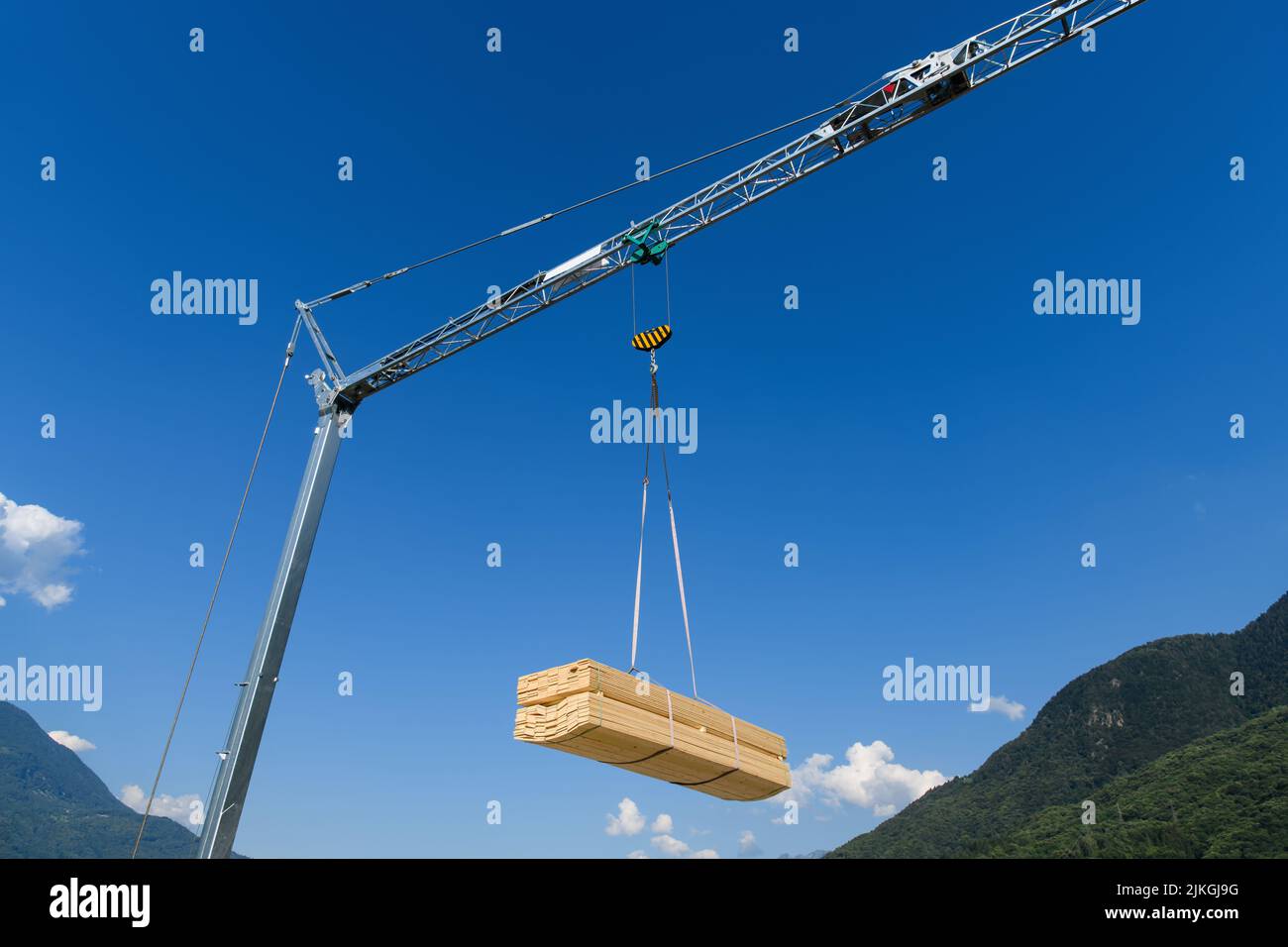 Gru da cantiere con carico appeso di asse in legno su un cielo blu Foto Stock