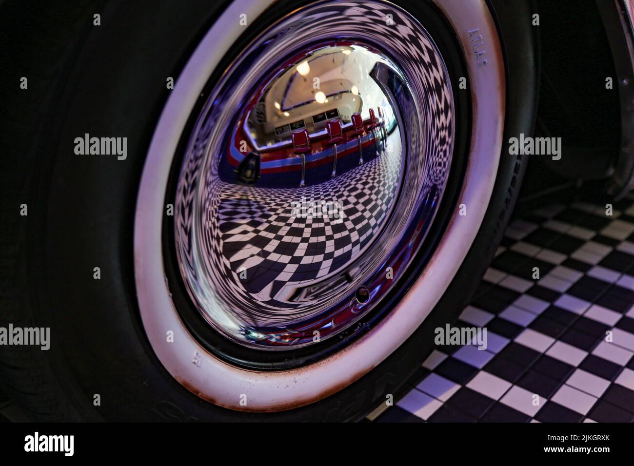 Un primo piano di un cappello a specchio di un classico pneumatico per auto con il riflesso del pavimento degli scacchi di un bar Foto Stock