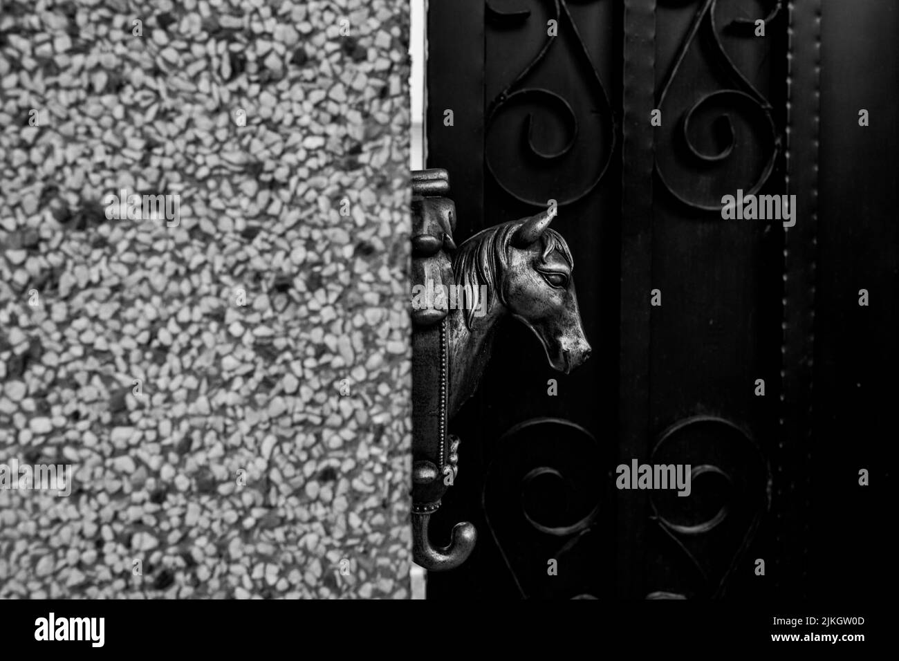 Un primo piano di una testa di cavallo di metallo attaccata al muro di un edificio con una porta sullo sfondo Foto Stock
