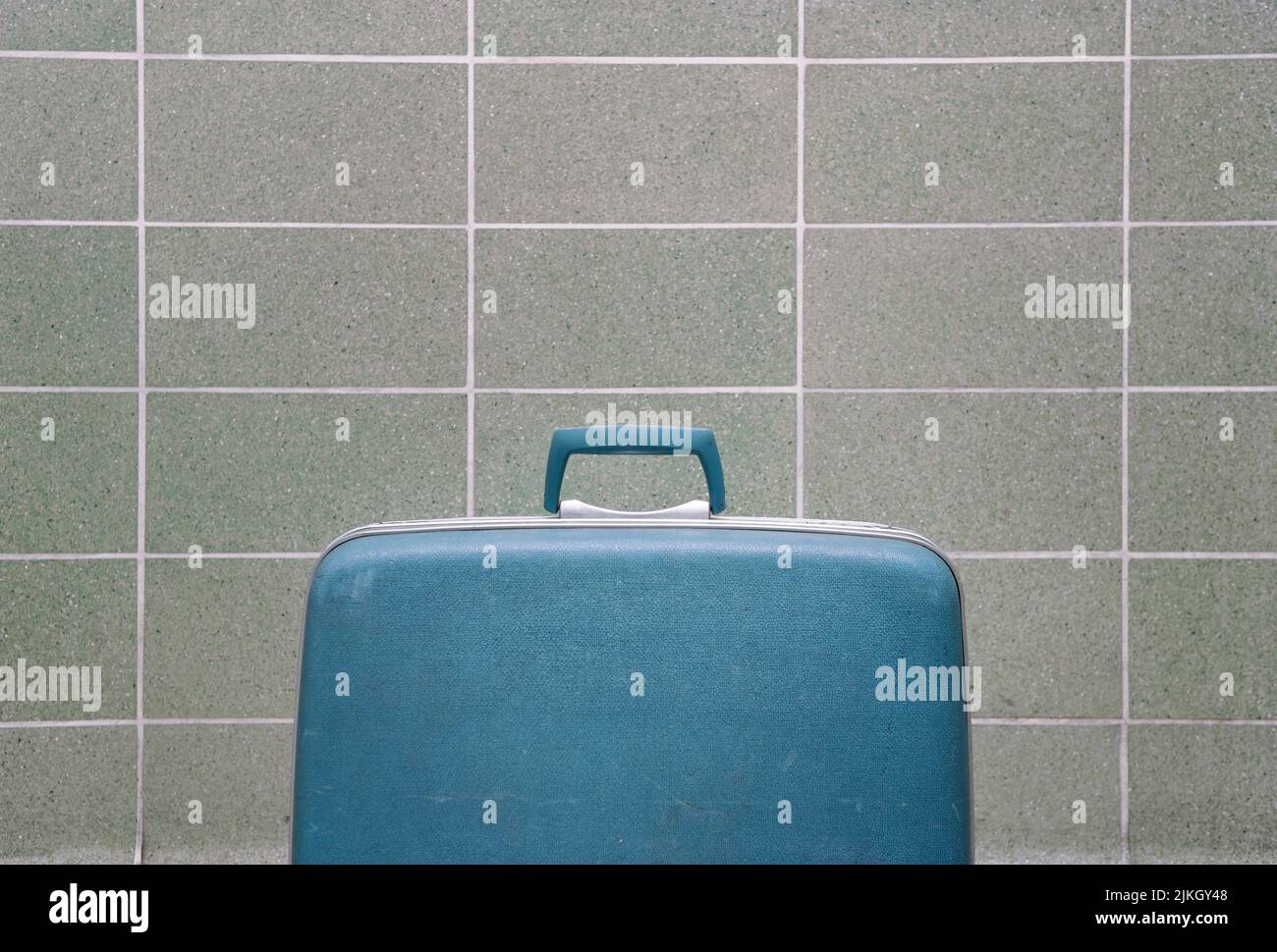La valigia vintage blu contro una moderna parete in piastrelle della metà del secolo Foto Stock