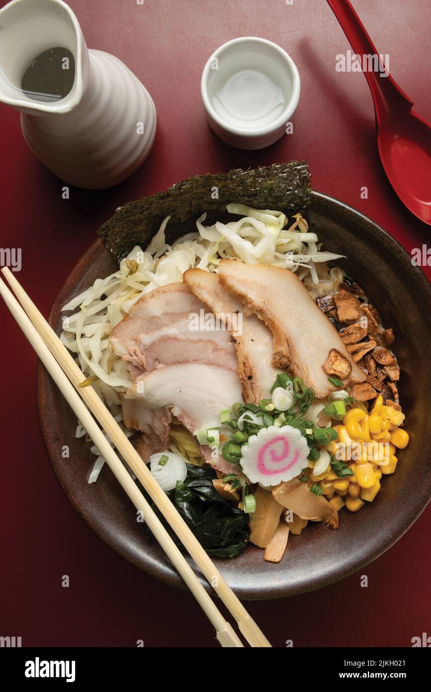 Una vista dall'alto delle tagliatelle di ramen giapponesi con bastoni di legno su un tavolo rosso Foto Stock