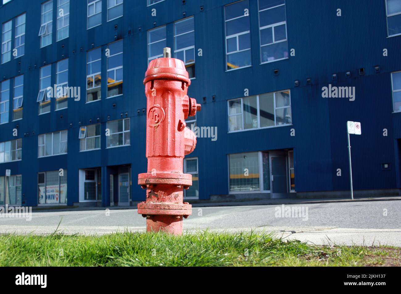 Un vecchio idrante rosso fuoco sul marciapiede erba per l'accesso antincendio di emergenza - edificio sullo sfondo Foto Stock